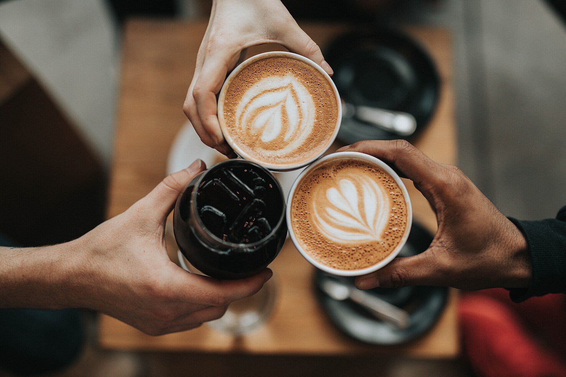 Manos brindando con tazas de café con arte latte sobre una mesa de madera