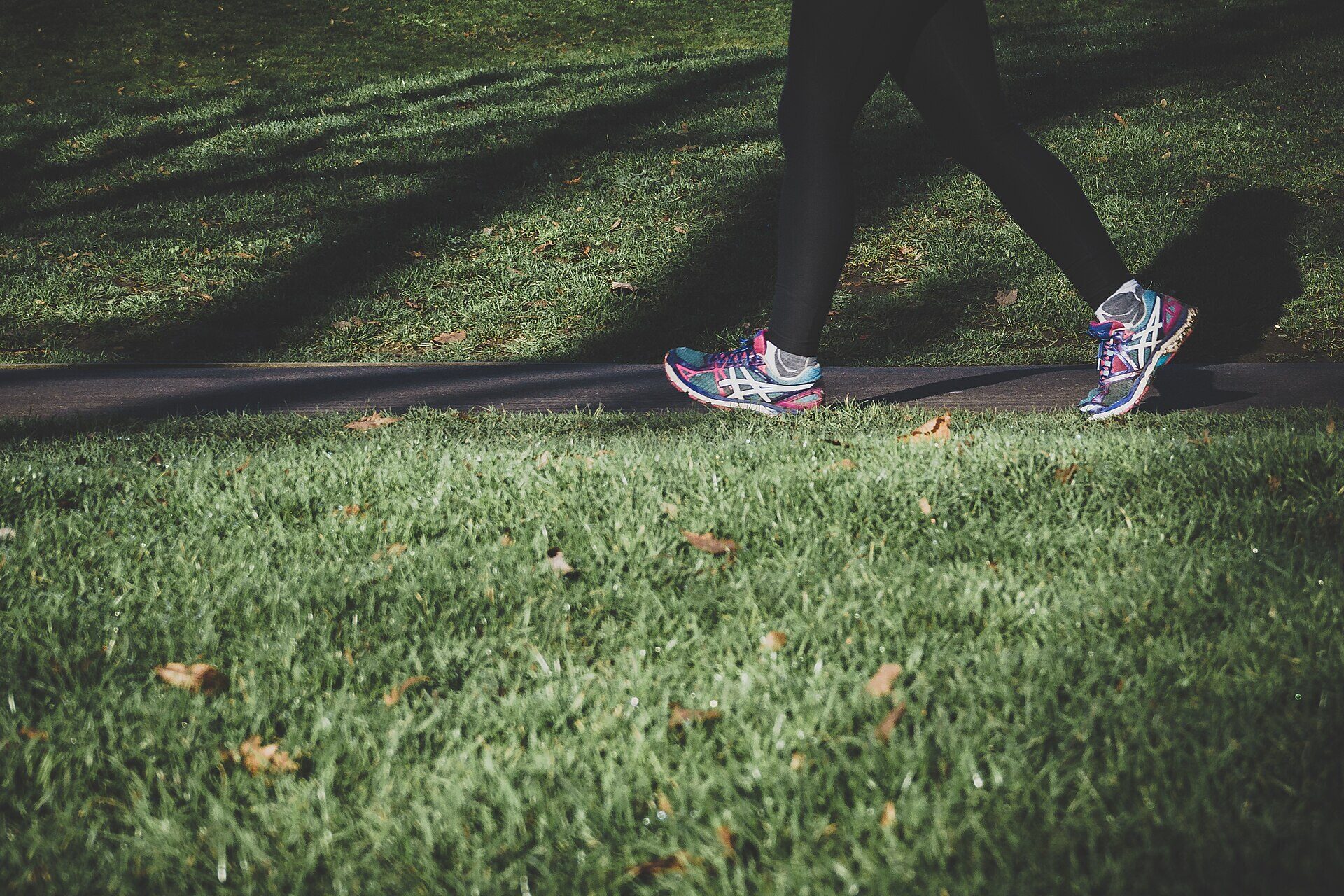 Piernas de una persona caminando sobre el pasto con tenis deportivos