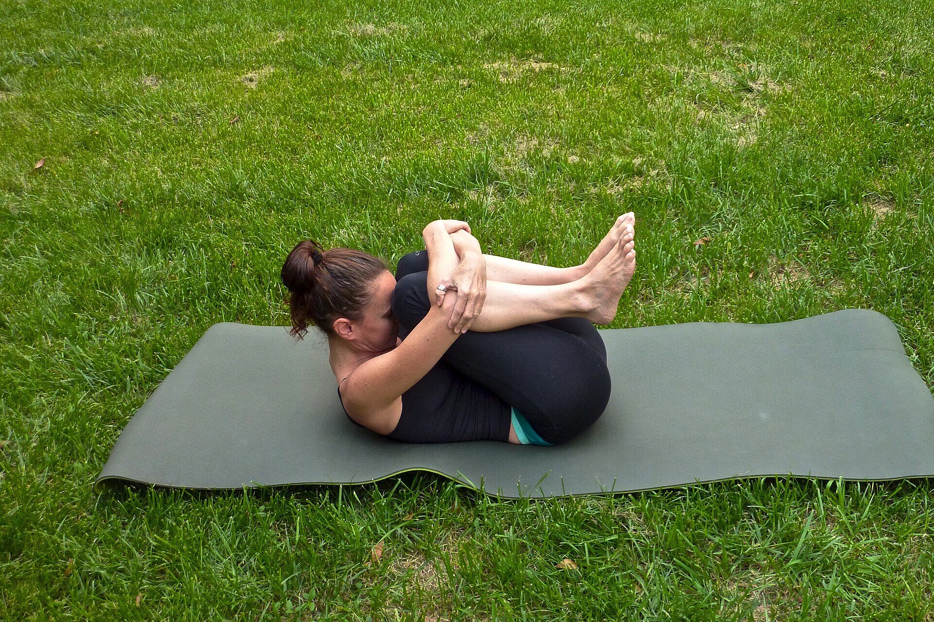 Persona practicando yoga sobre un tapete en el pasto